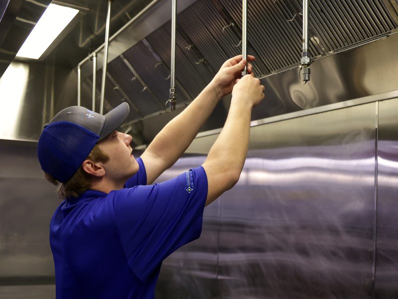 Technician adjusting kitchen hood suppression piping